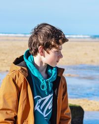 Teenage boy standing at beach against sky