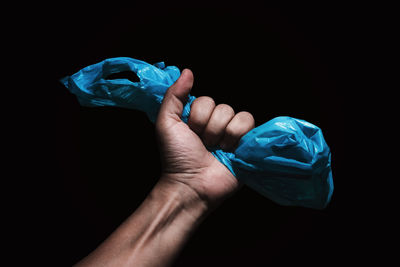 Close-up of human hand holding plastic against black background