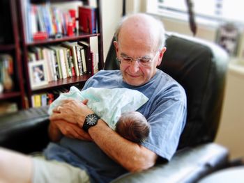 High angle view of grandfather holding baby while sitting on chair at home