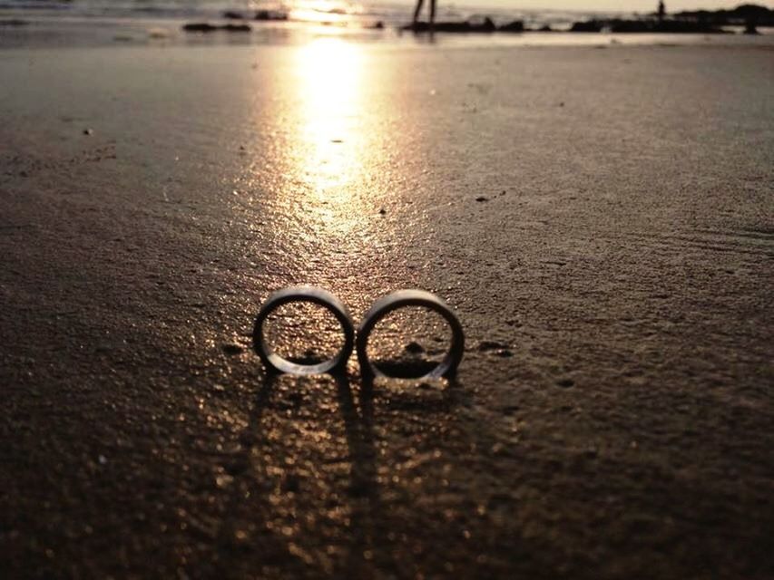 surface level, water, street, asphalt, beach, selective focus, reflection, road, wet, circle, outdoors, transportation, no people, cobblestone, bicycle, sand, close-up, tranquility, nature, sunlight