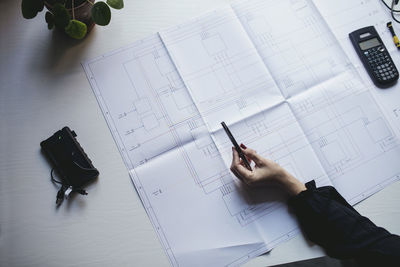 Cropped hand of businesswoman with blueprint on desk