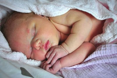 Close-up of new born baby wrapped in blanket sleeping on bed
