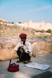 Man sitting on retaining wall against sky