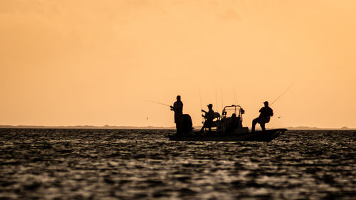 Silhouette people on sea against orange sky