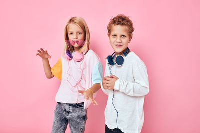 Portrait of sibling wearing headphones against colored background