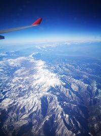 Aerial view of airplane wing over landscape against blue sky