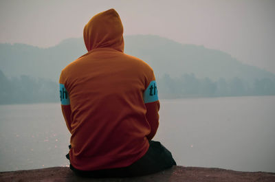 Rear view of man looking at lake against sky