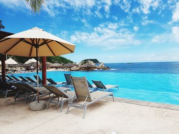 Lounge chairs by swimming pool at beach against sky