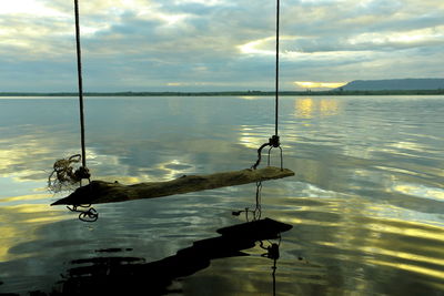 Wooden swing hanging over lake against sky during sunset