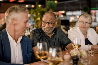 Smiling senior man talking with male friend while sitting by woman in restaurant