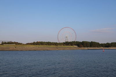 Ferris wheel by river against blue sky