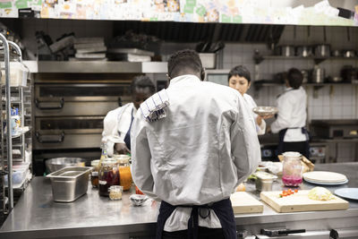 Rear view of chef working with colleagues in kitchen of restaurant