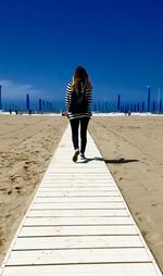 Rear view of woman walking on pier at beach