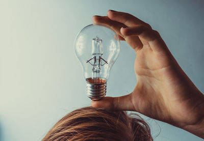 Close-up of hand holding light bulb on head against white background