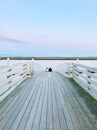 Couple sitting on footbridge against lake