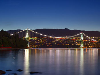 Illuminated bridge over river against sky at night