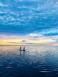 People paddleboarding in sea against sky during sunset
