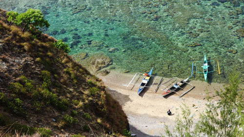 High angle view of person sitting by outrigger boats moored on shore at beach