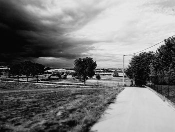 Empty road amidst houses against cloudy sky