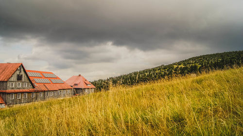 Houses by grassy field against cloudy sky