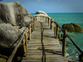 Footbridge by rocks over sea against sky