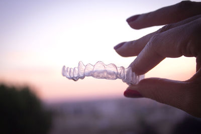 Cropped hand of woman holding dental aligner against sky during sunset