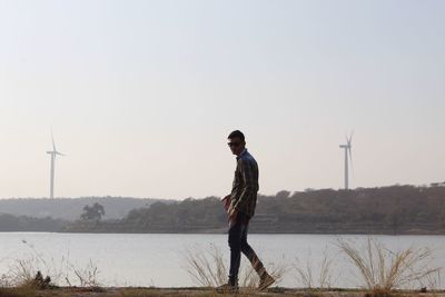 Full length of man walking on field by river against clear sky