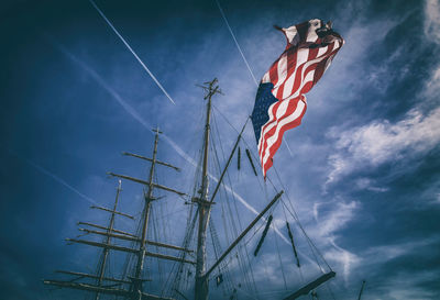 Low angle view of american flag waving on mast against cloudy sky