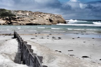 Scenic view of sea by rock formations against cloudy sky