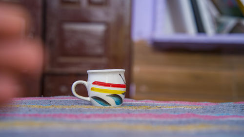White porcelain tea cup with red and yellow line decoration and a sofa, on home background.
