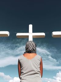 Low angle view of woman standing against cross during sunny day