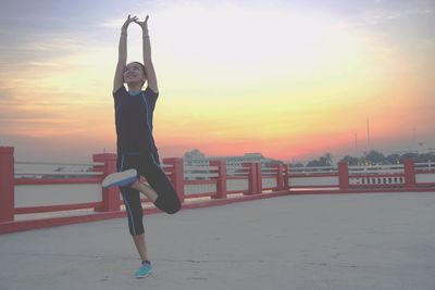 Smiling woman with arms raised standing on walkway during sunset