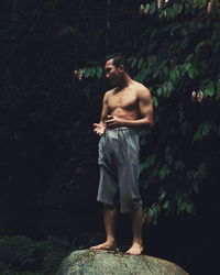 Full length of shirtless man standing in forest