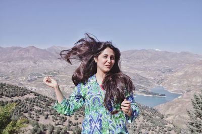 Beautiful young woman standing on mountain against clear sky