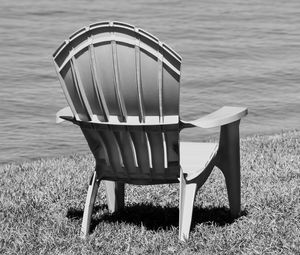 Empty chair on field by lake