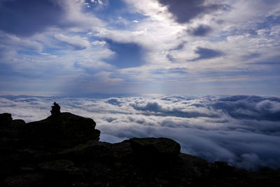 Person sitting on mountain against cloudy sky