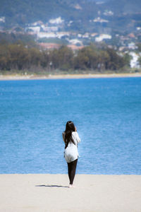 Rear view of woman standing on sand against sea at beach