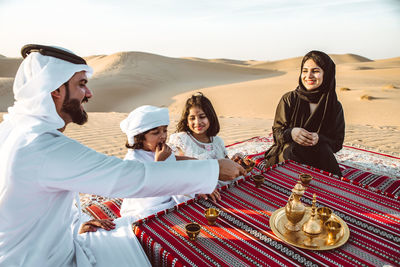 Happy family having tea on carpet at desert