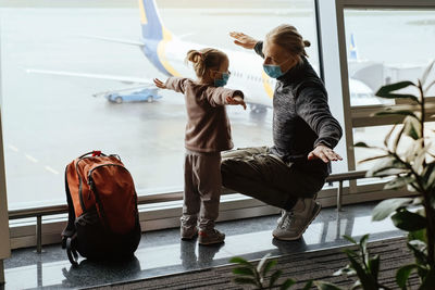 Man with girl ready to fly by airplane and the airport. father and child looking though the lounge