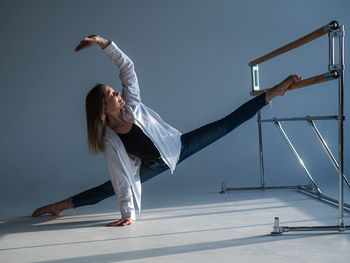 Caucasian woman in casual clothes pulls the split at the ballet barre. 