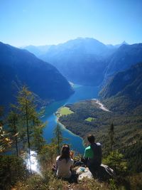 Rear view of couple sitting on mountain during sunny day