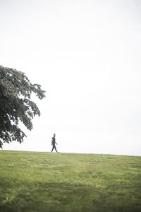 Mid distance view of young man walking on grassy field against sky
