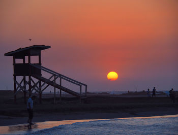 Silhouette people standing on beach against sky during sunset