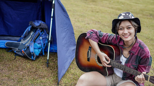 High angle portrait of woman playing guitar while sitting by tent