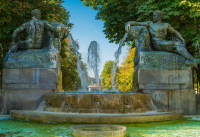 Statue by fountain against trees