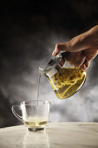 Midsection of person pouring drink in glass on table