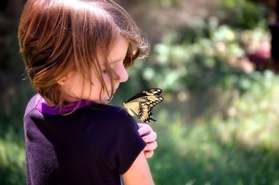 Rear view of girl looking at butterfly on shoulder