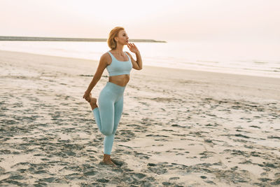 A woman stretches her leg on the beach, prepares for exercises or finishes a workout