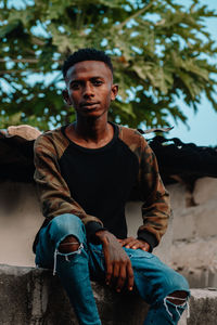 Portrait of young man sitting on retaining wall