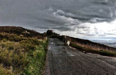 Road passing through landscape against cloudy sky